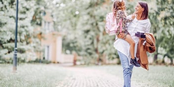 mom carrying daughter in one arm while walking with coffee in her other hand