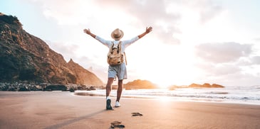 person walking on a beach at sunrise raising their arms up with joy