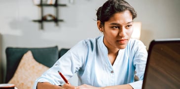 person looking at their computer and writing something down on paper