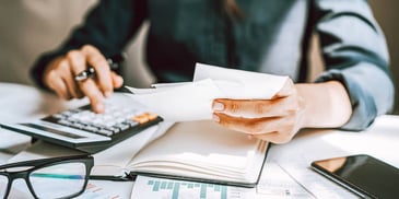 woman using a calculator and holding notes at a desk