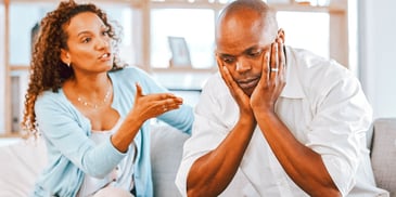 sad man holding his face in his hands while his wife lectures him
