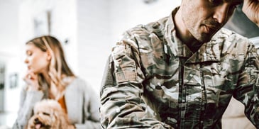 upset military servicemember and woman sitting apart on a bed