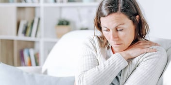 woman holding her tense shoulders in pain 