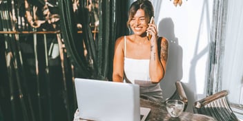 woman sitting outside talking on the phone and looking at her laptop
