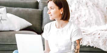 tattooed woman sitting on floor and working on her laptop
