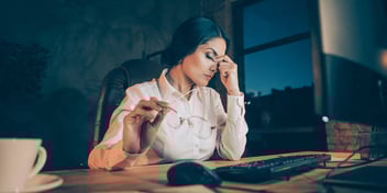 exhausted women sitting at her desk rubbing her forehead