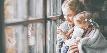 Two caucasian children looking out window together.
