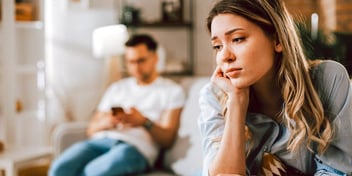 unhappy younger woman sitting apart from her distracted husband who is ignoring her