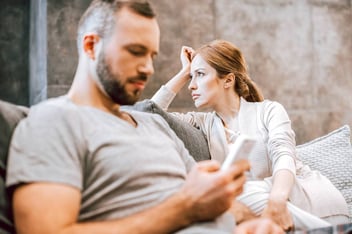 unhappy couple on couch woman daydreaming man looking at his phone