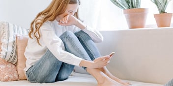 upset woman on a couch scrolling through her phone