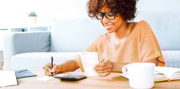woman smiling while doing calculations and writing notes