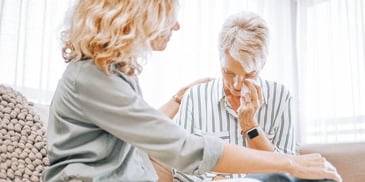 senior woman crying next to a younger blonde woman who is comforting her