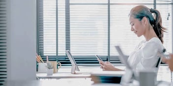 woman sitting down at her desk looking at her phone