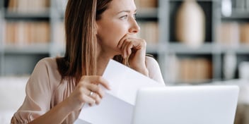Woman holds papers in front of her laptop
