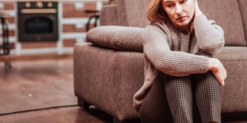 Woman sits sadly in front of her couch