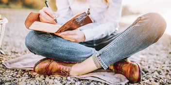 Woman sits on the ground writing in her journal