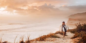 woman walking along a beach with a surfboard in California