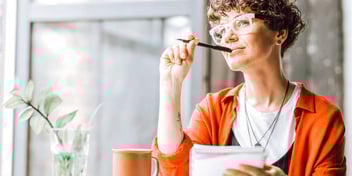 woman thinking as she takes notes in a notebook