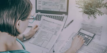 woman going over tax forms and inputing numbers into a calculator