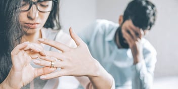 woman taking off her wedding ring as husband holds his face behind her