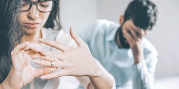 woman taking off her wedding ring as husband holds his face behind her