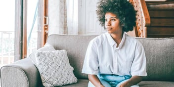 Young black woman sitting on a couch staring off into the distance.