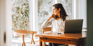 Young woman sitting at table with laptop staring out window