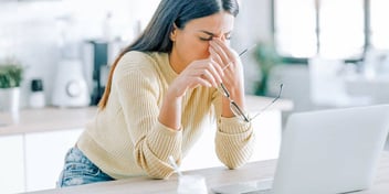 Young woman holding bridge of nose while holding glasses feeling distraught