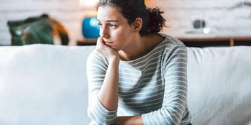 Young woman sitting on couch looking distraught with head in hand