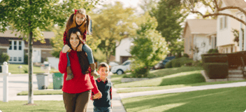 mom walking with young daughter sitting on her shoulders and holding son's hand